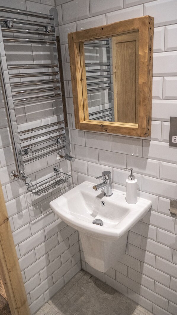 A bathroom with a white sink, chrome faucet, and a wooden-framed mirror. - Trail Lodge (Ballasalla)