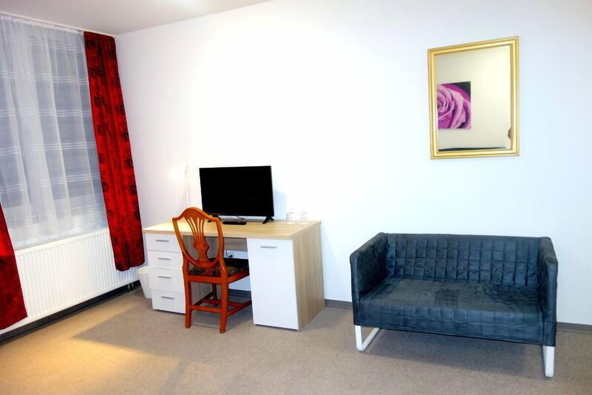 A room with a desk, chair, and a dark-colored sofa.