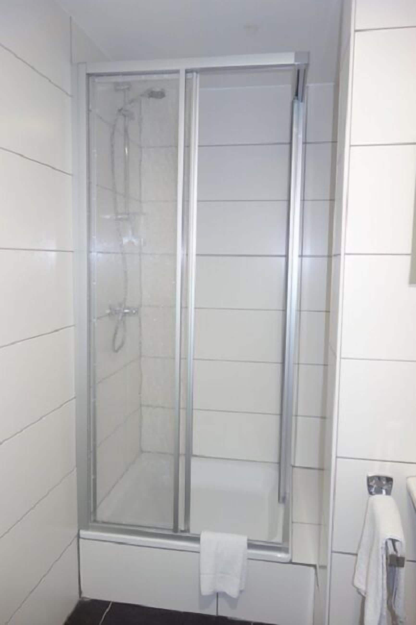A bathroom with a glass-enclosed shower, white tiled walls, and a black countertop.