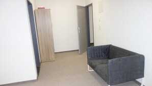 A hallway with a dark grey upholstered chair, a wooden wardrobe, and a door leading to another room. - Budget Hotel Ludwigshafen (Ludwigshafen)