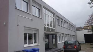 A modern building with multiple windows and a car parked in front. There are two blue trash bins labeled "Altpapier" near the entrance. - Budget Hotel Ludwigshafen (Ludwigshafen)