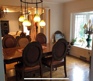 A dining room with a wooden table and chairs, a chandelier, and a window with plants.