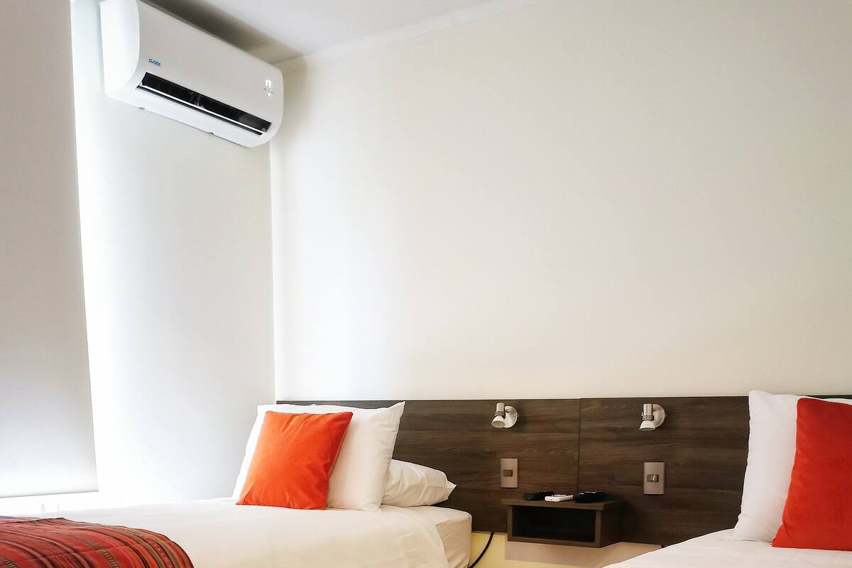 Een hotelkamer met twee bedden, elk met een ander beddegoed, een nachtkastje met een lamp en een airconditioning aan de muur.