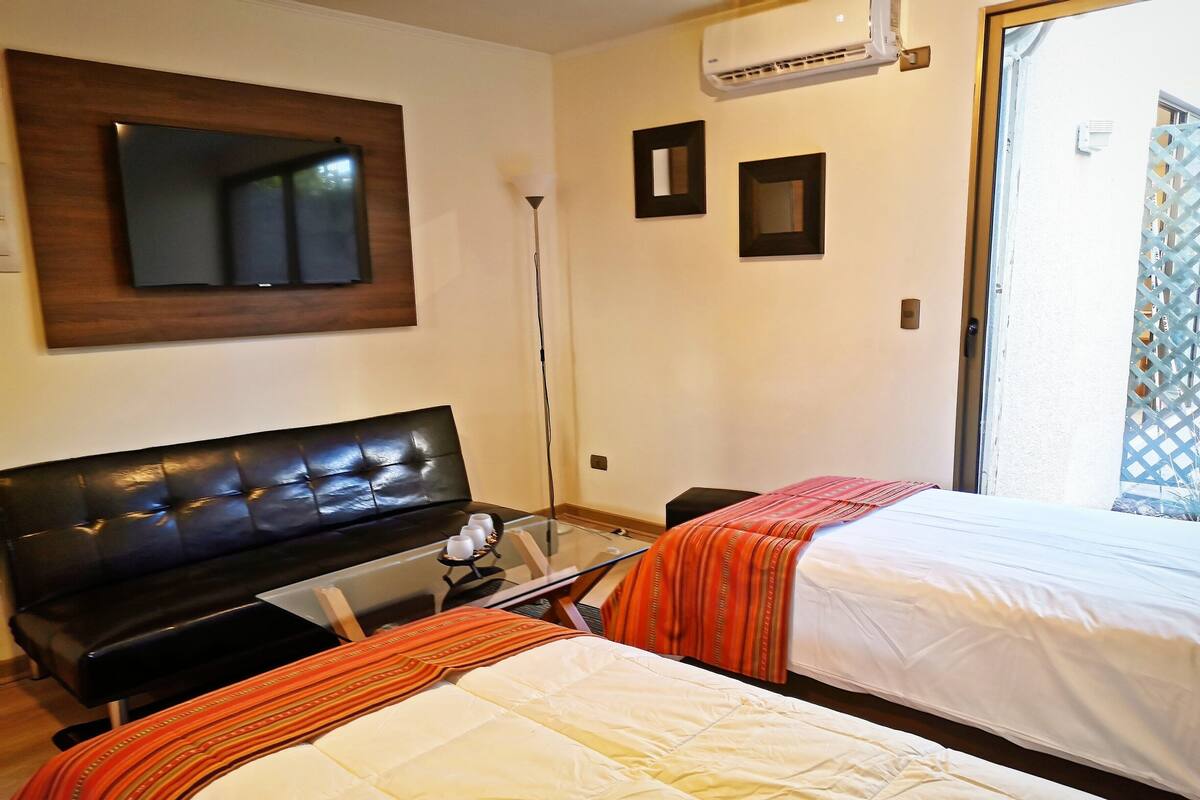 Een hotelkamer met een groot bed, een kleiner bed, een bank, een televisie en een airconditioning.
