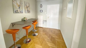 A dining area with a wooden herringbone floor, a white door, and three orange bar stools. - Check Point - Syngrou Fix (Athens)