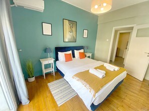 A neatly arranged bedroom with a large bed, bedside tables, a nightstand, and a potted plant. - Check Point - Syngrou Fix (Athens)
