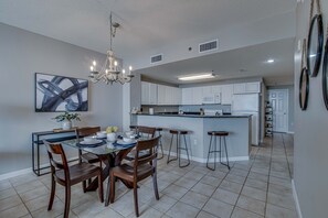 A modern kitchen with white cabinets, a central island, and a dining area with wooden chairs and a glass table.