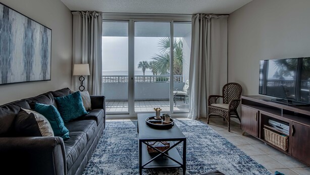 Ein modernes Wohnzimmer mit einer Couch, einem Couchtisch, einem Fernseher und einem Balkon mit Vorhängen.