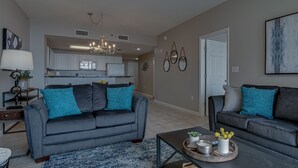 Ein modernes Wohnzimmer mit einem grauen Sofa, einem Couchtisch mit Dekoration und einer Küche im Hintergrund.