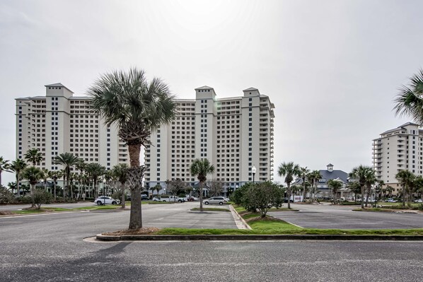 A multi-story hotel with a central courtyard, surrounded by palm trees and parked cars.