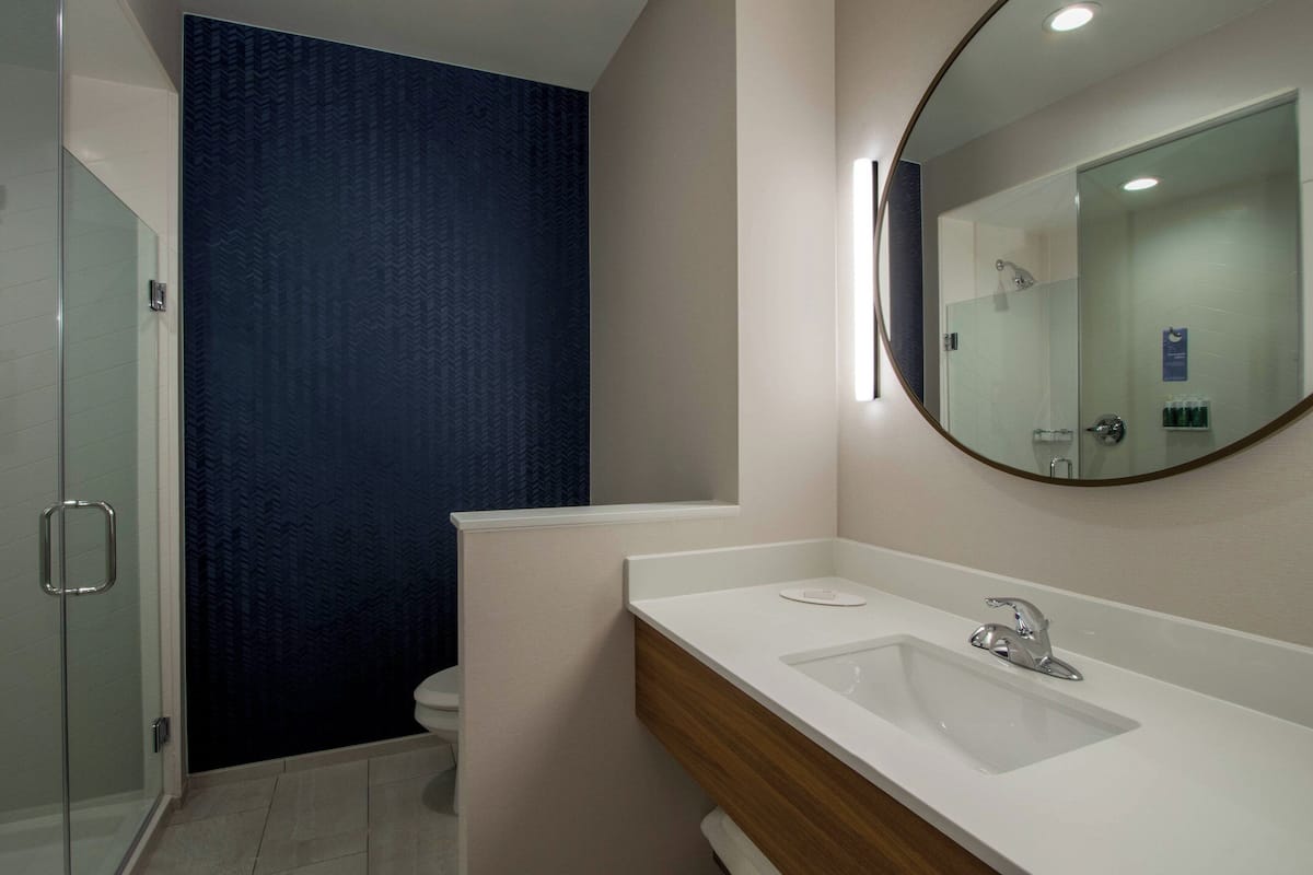 Un baño moderno con cabina de ducha de vidrio, un lavamanos blanco con mueble de madera y un espejo grande.