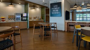A modern cafe with wooden furniture, a chalkboard sign, and a beverage dispenser.