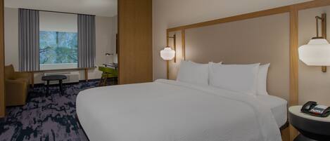 A hotel room with a large bed, a desk, a chair, a window with curtains, and a lamp.