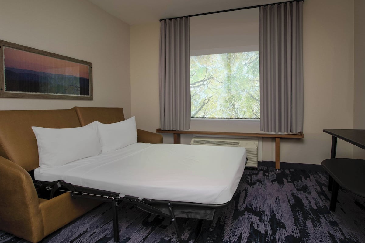 Una habitación de hotel con cama, sofá, mesa y ventana con cortinas.