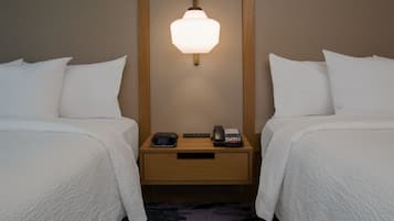 Une chambre d’hôtel avec deux lits, une table de chevet avec une lampe, un téléphone et une horloge numérique.