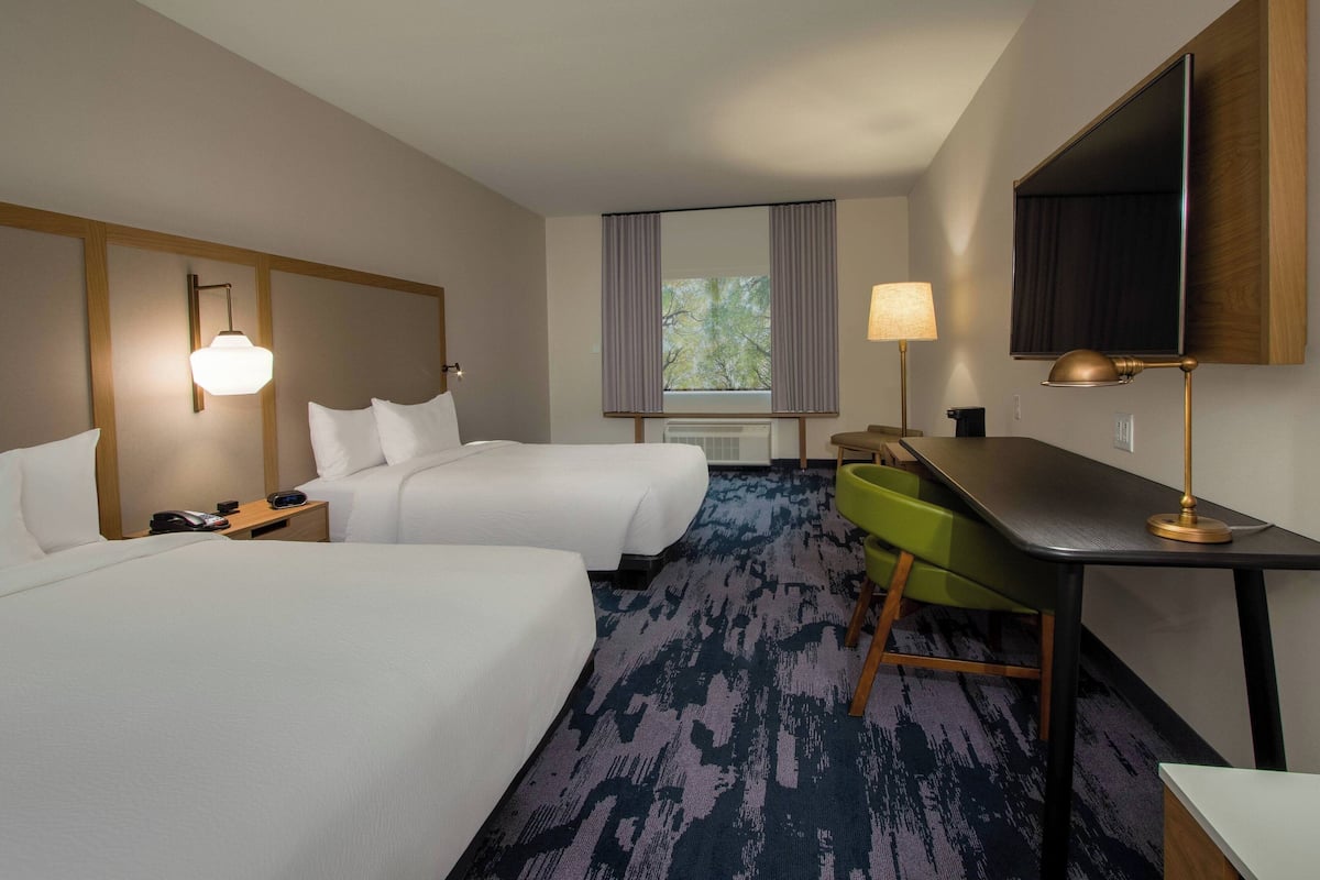 Habitación de hotel con dos camas, un escritorio, una silla, un televisor y una ventana con cortinas.