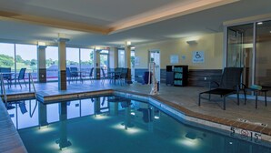 A swimming pool area with clear poolside chairs, a pool lift, and a view of the surrounding landscape.