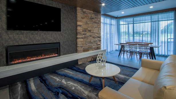 A modern living room with a fireplace, a flat-screen TV mounted on the wall, a stone accent wall, a round coffee table, and a sofa. - Fairfield Inn & Suites Duncan (Duncan)