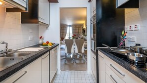 A modern kitchen with a central island, stainless steel appliances, and a dining area with a view. - Modern 2 bedroom in Kensington (London)