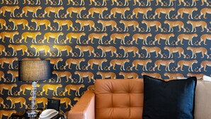A room with a leopard print wallpaper, a brown leather sofa, a black pillow, a lamp, and a small table with a book and a decorative item. - Modern 2 bedroom in Kensington (London)