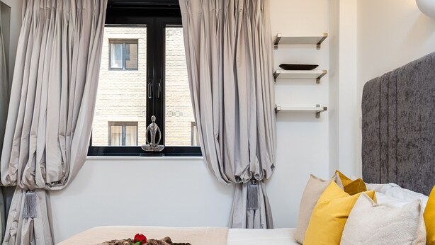 A bedroom with a bed, curtains, a window, and a view of a building. - Modern 2 bedroom in Kensington (London)