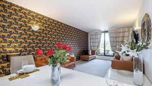 A dining area with a white table set for two, a vase with red flowers, and a mirror on the wall. - Modern 2 bedroom in Kensington (London)