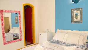A hotel room with a bed, a red door, a small white appliance, and a mirror with a red frame. - Pousada Florescer (Paraty)