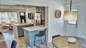 A modern kitchen with a central island, a dining area with a round table, and a living space with a sofa and a TV.
