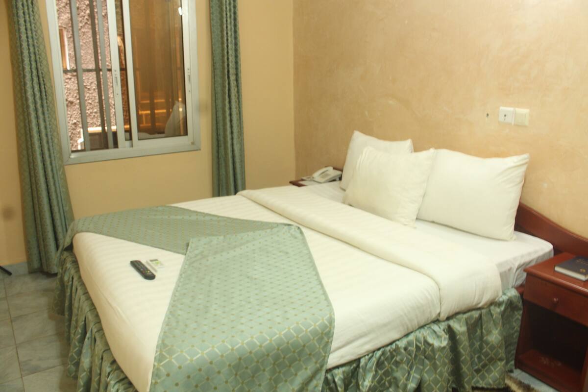 A hotel room with a bed, a nightstand, a telephone, and a window with curtains.