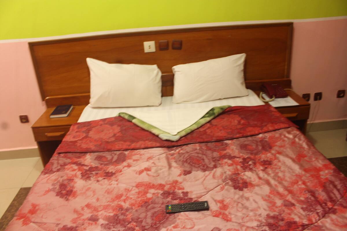 A bed with a floral bedspread, a remote control, and a smartphone on the nightstand.