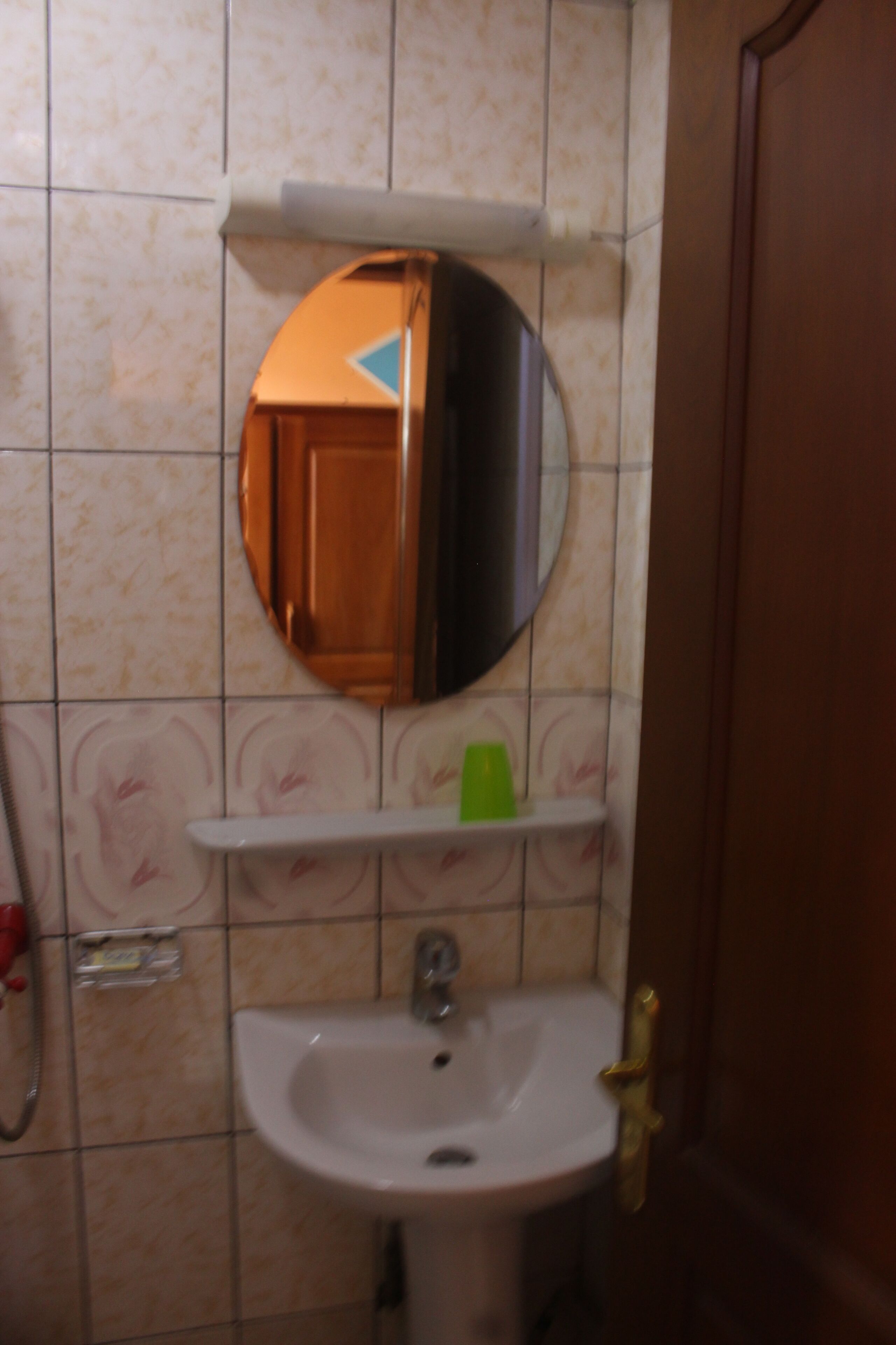 Een badkamer met een wastafel, spiegel en een groene beker op een plank.