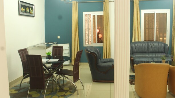 A dining area with a table and chairs, a sofa, and a window with curtains. - Florencia Hotel (Yaoundé)