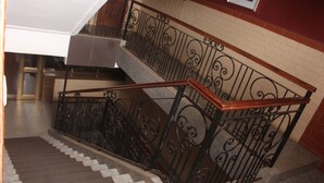 A staircase with a wooden handrail and black wrought iron balustrade. - Florencia Hotel (Yaoundé)
