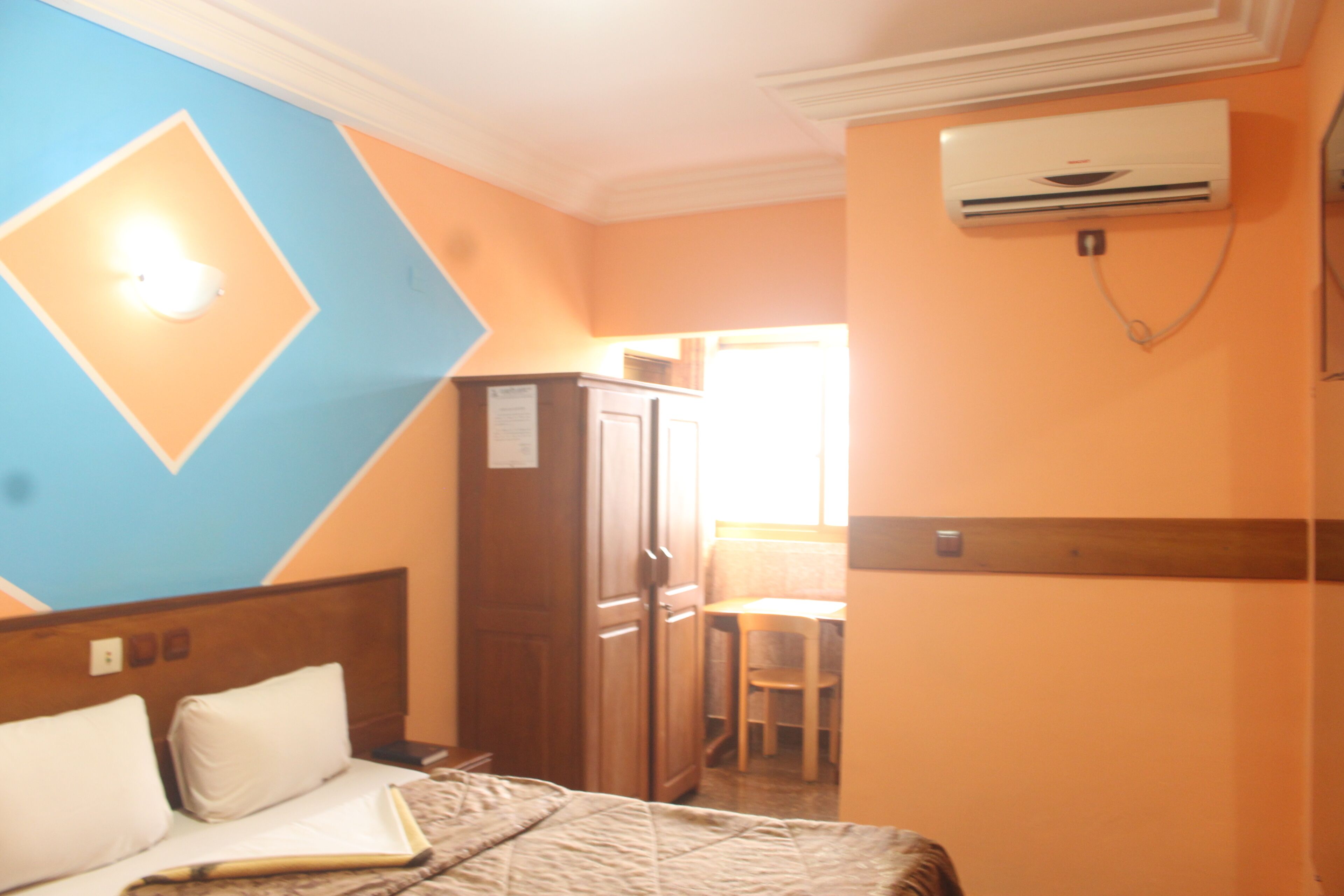 Een hotelkamer met een bed, een bureau en een stoel. Er is een airconditioner aan de muur.