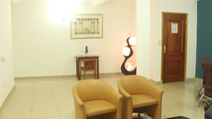 A room with two armchairs, a small table with a vase, a framed picture on the wall, and a door in the background. - Florencia Hotel (Yaoundé)
