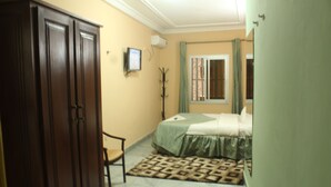 A bedroom with a bed, a wardrobe, a coat rack, and a window with curtains. - Florencia Hotel (Yaoundé)