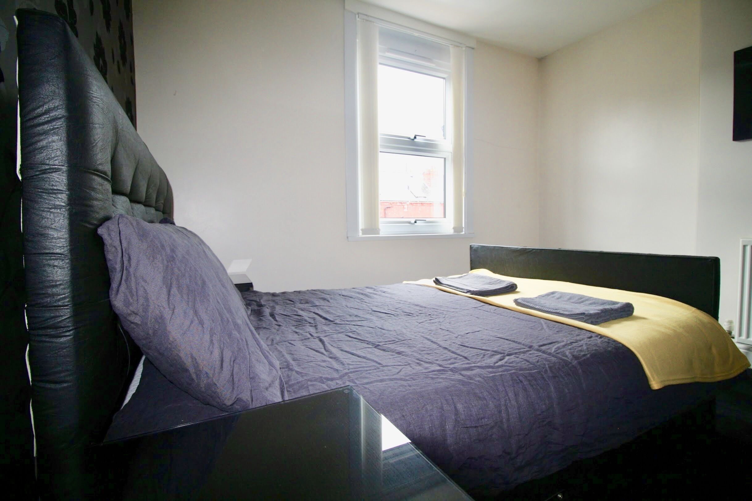 Un dormitorio con cama, ventana y una mesa negra.