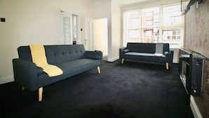 A living room with two dark sofas, a flat-screen TV, and a patterned wallpaper.