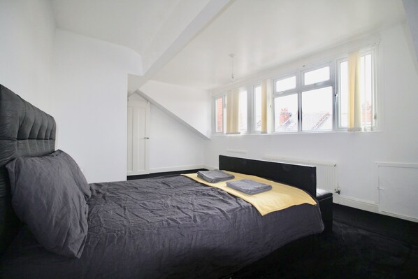 A bedroom with a large bed, a window with curtains, and a radiator.