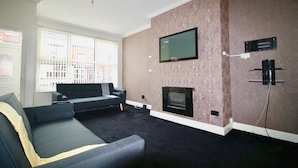 A living room with a fireplace, a flat-screen TV mounted on the wall, and a sofa.