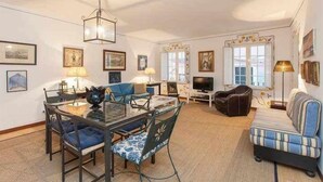 A living room with a glass dining table, blue upholstered chairs, a striped sofa, and a television. - Elegant in Alfama with Terrace and FREE parking. (Lisboa)
