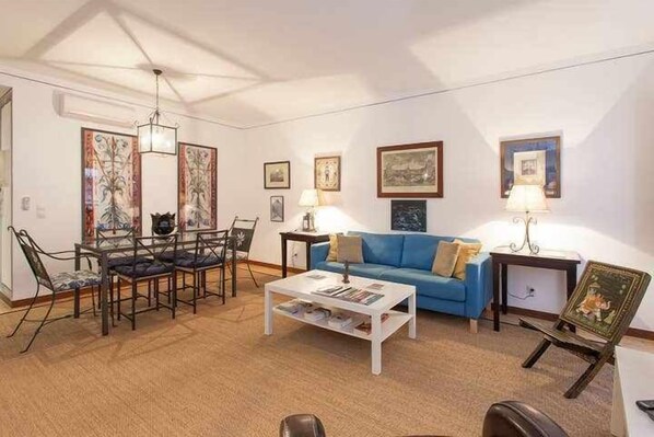 Uma sala de estar com um sofá azul, uma mesa de centro e um espaço de jantar com cadeiras e uma mesa.