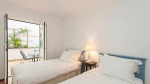 A hotel room with two beds, a small table, a chair, and a balcony with a view. - Elegant in Alfama with Terrace and FREE parking. (Lisboa)