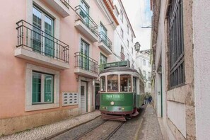 Eine grüne Straßenbahn mit der Aufschrift "TRAM TOUR", die eine enge Straße entlangfährt, gesäumt von Gebäuden mit Balkonen und Fenstern.