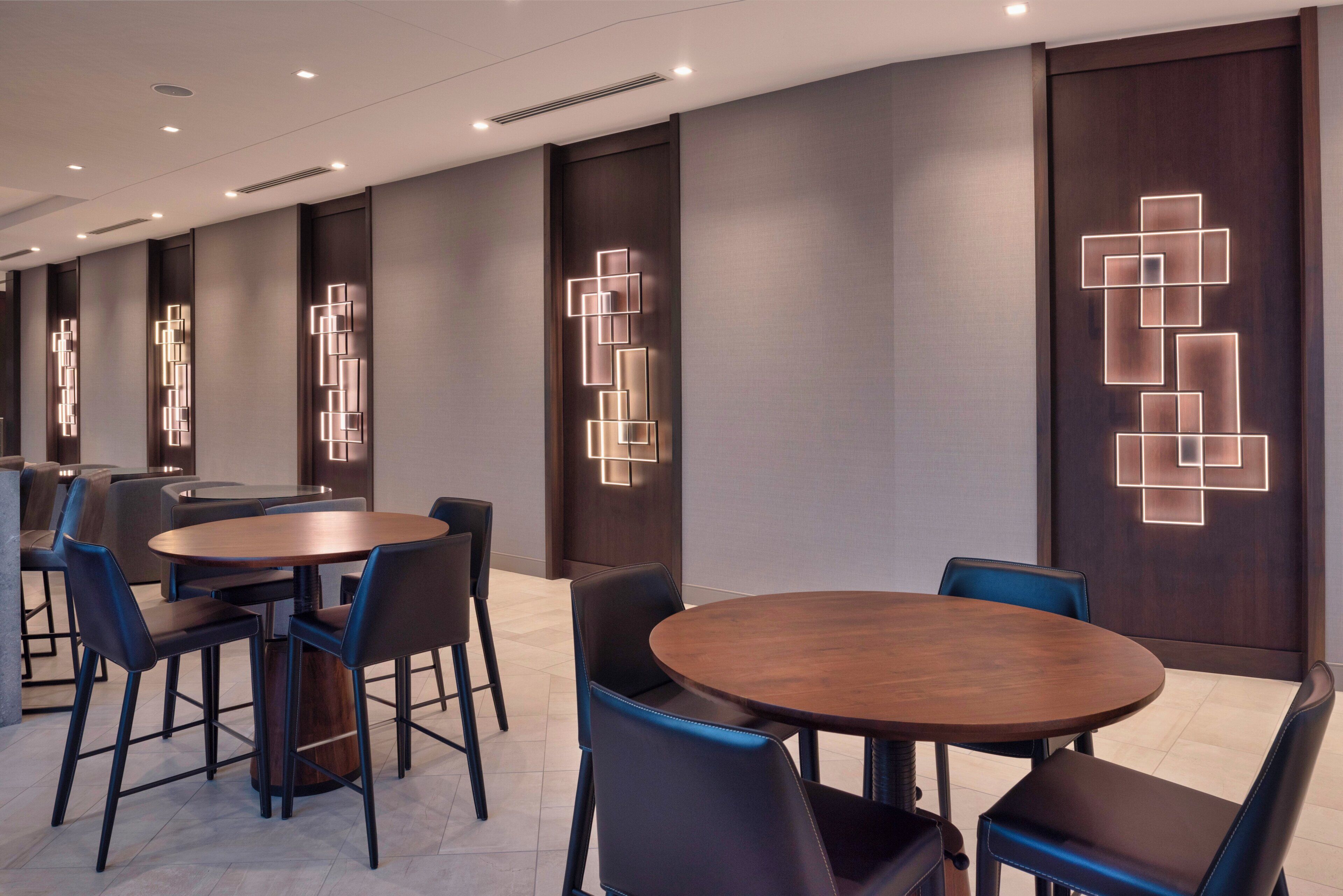 A modern hotel lobby with round tables and chairs, recessed lighting, and decorative wall panels.