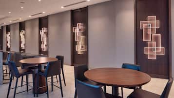 A modern hotel lobby with round tables and chairs, recessed lighting, and decorative wall panels.