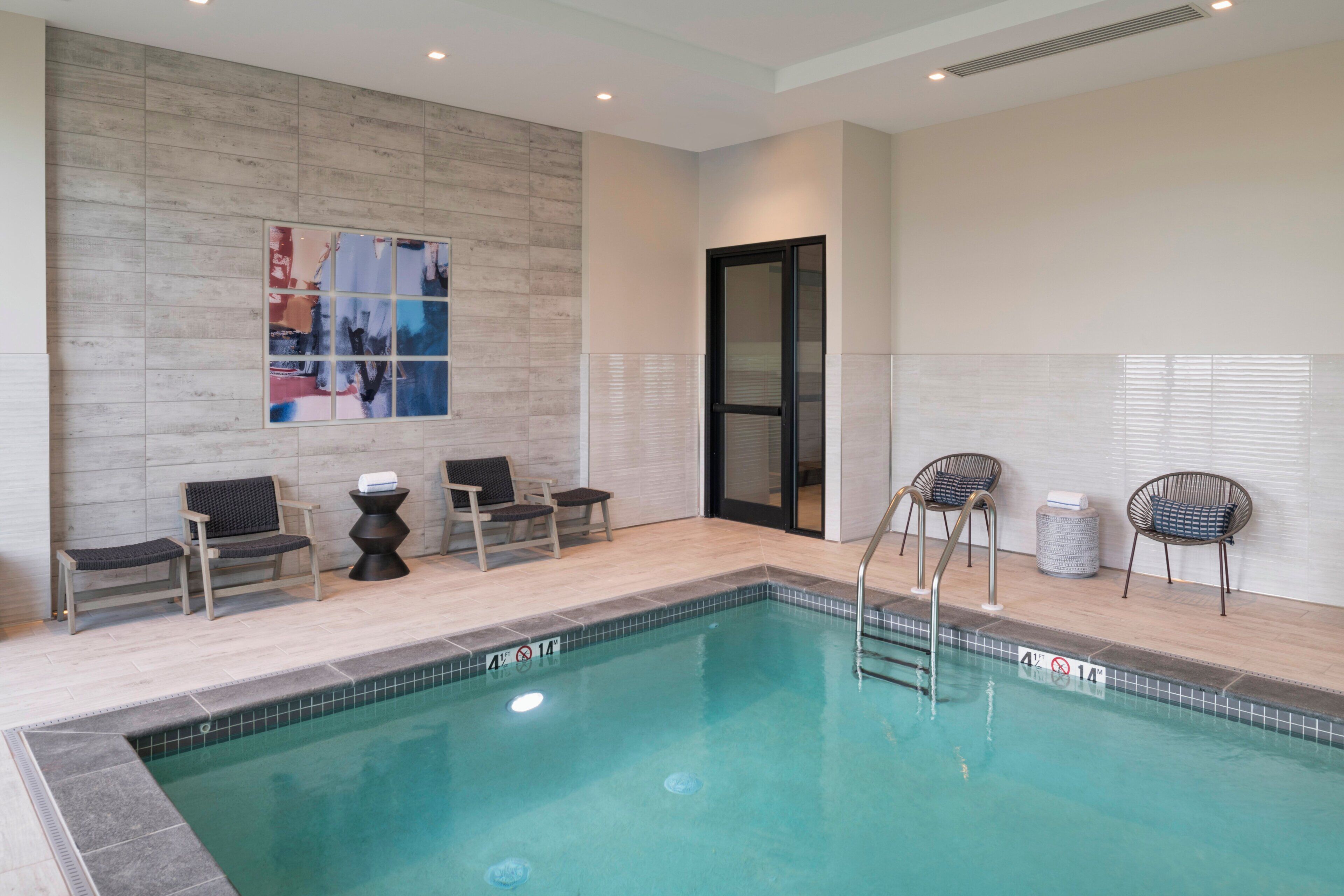 Uma piscina com borda revestida em azulejos, um banco e duas cadeiras.