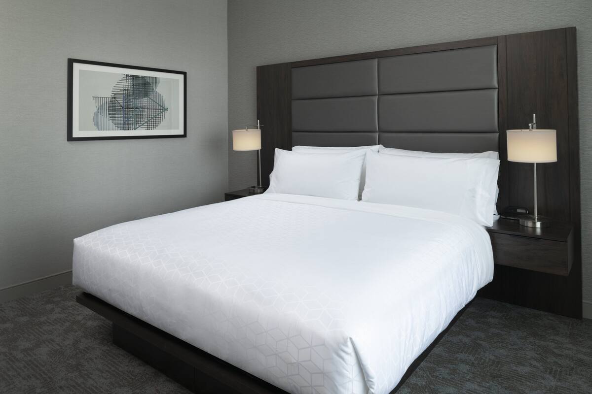 A neatly made bed with a headboard, two bedside lamps, and a framed picture on the wall.