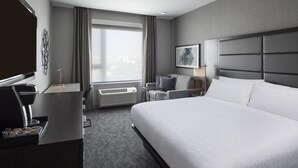 A modern hotel room with a large bed, a desk with a coffee machine, a chair, a TV, and a large window with curtains. - Holiday Inn Express Boston Logan Airport - Revere by IHG (Revere)