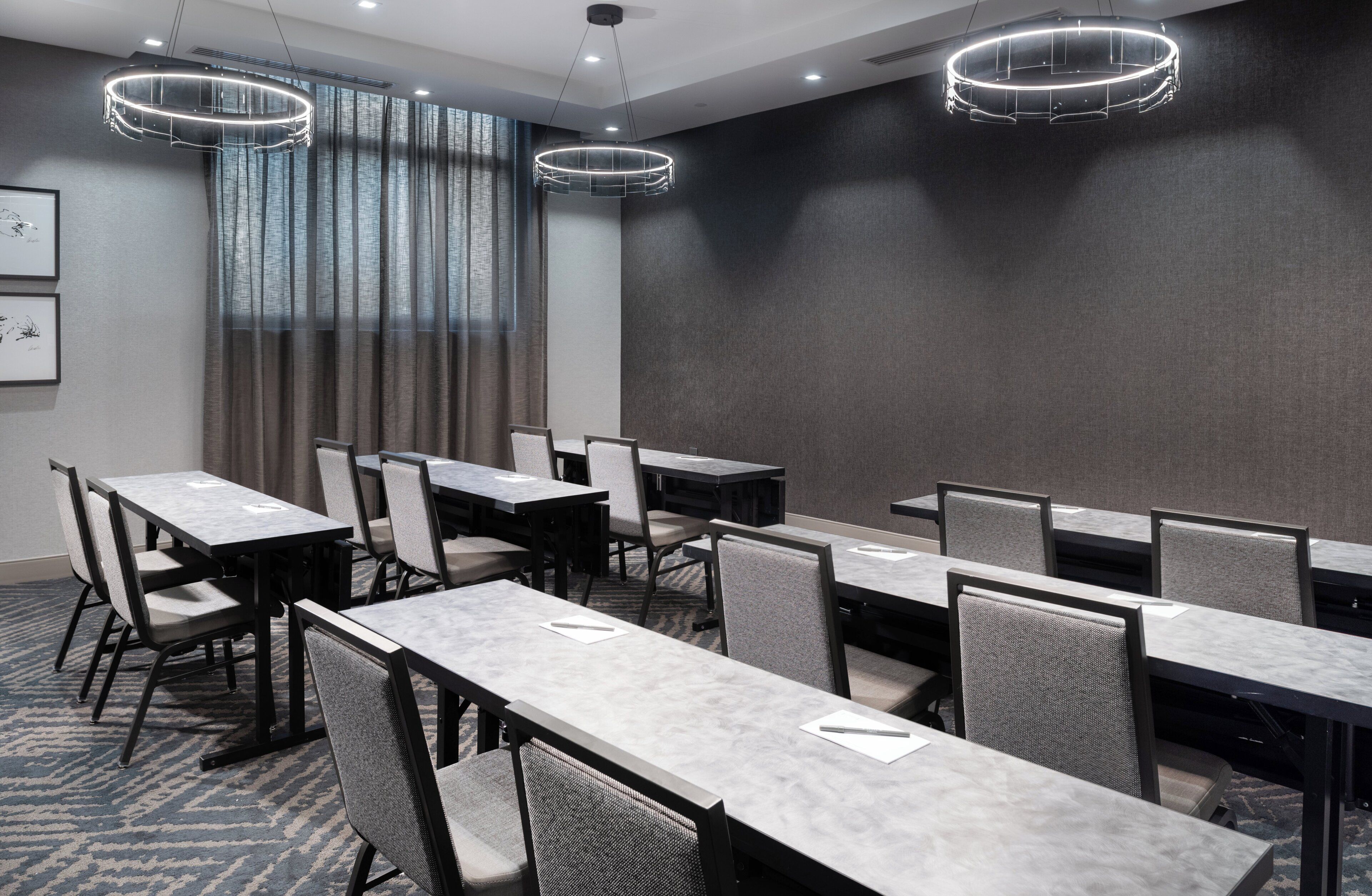 A conference room with multiple tables and chairs, large windows with curtains, and modern lighting fixtures.
